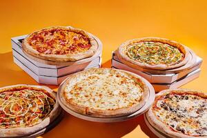 Five delicious pizzas with various toppings arranged against a bright orange background photo