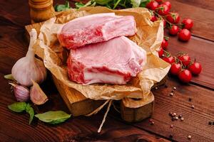 Fresh pork chops arranged on a wooden board with herbs and cherry tomatoes in a rustic kitchen setting photo