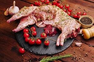 Freshly prepared rabbit meat garnished with herbs and cherry tomatoes on a wooden table photo