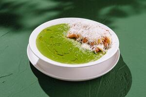 Delicious green soup served with crispy toppings and cheese in a bright setting photo