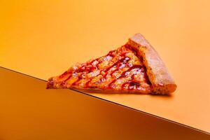 Slice of pizza resting on a vibrant orange surface showcasing melted cheese and toppings during a casual meal time photo