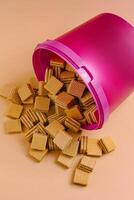 Waffle biscuit pieces spilled from a pink container on a peach-colored surface photo