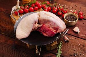 Fresh meat cut displayed on a wooden table with tomatoes, herbs, and spices in a rustic kitchen setting photo