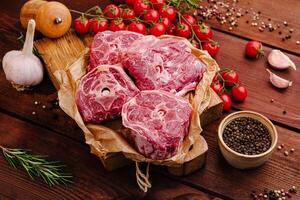 Fresh cuts of meat arranged on a wooden board with herbs, spices, and cherry tomatoes ready for cooking photo