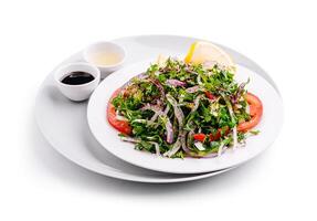 Fresh mixed salad served on a white plate with dressing choices and lemon wedge photo