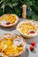 Assorted snacks served in baskets with dips on a table surrounded by greenery photo