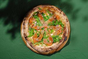 Rustic wood-fired pizza topped with fresh arugula and smoked salmon on green background photo