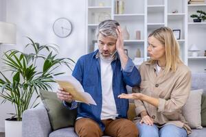 A stressed couple reviewing their finances and bills while sitting on a sofa at home. The image conveys worry, stress, and financial problems. photo
