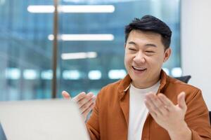 Asian man businessman engaged in call in office. He appears happy and communicative, suggesting positive interaction and successful business meeting. His open posture conveys enthusiasm. photo