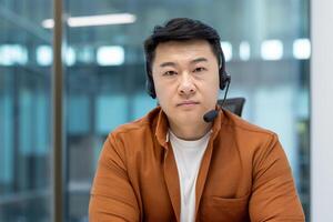 Asian man working in an office while using a headset for communication and teamwork. photo