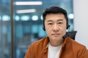 Asian man in office setting wearing headset, showcasing professionalism, communication skills, and business environment presence. Image captures calm and confident demeanor during work interaction. photo