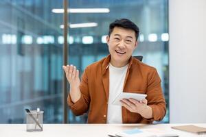 Asian man and mature businessman looking at the camera and communicating during a call using a smartphone, displaying a cheerful and engaging demeanor in a professional office setting. photo