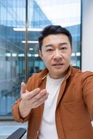 Asian mature businessman engaging in a call, looking at the camera talking. Located indoors with a professional ambiance, conducting a serious and compelling conversation for communication photo