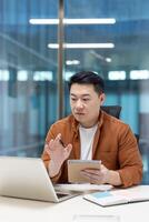 Asian man mature businessman engaged in remote work, taking notes, and communicating online in a modern workspace. Represents productivity and digital work environments. photo