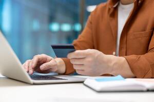 Asian businessman using credit card and laptop for online payment. Image captures essence of modern finance, technology, e-commerce, and business transactions with focus on convenience. photo