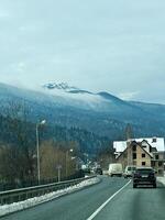 Scenic winter road with mountain view and rural architecture under cloudy sky photo