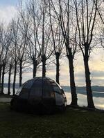 Geodesic dome near a serene riverside with tree rows during sunset photo