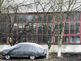 Covered car near factory building with bare trees surrounding the scene photo