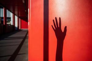 Death shadow cast by hand reaching across red wall in urban hallway symbolizing life's transience photo