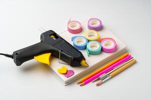 Crafting supplies for creative projects featuring a hot glue gun and colorful tape on a work surface photo