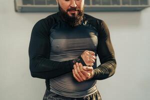 Man adjusts wrist support while preparing for workout in a gym setting with fitness equipment in the background photo