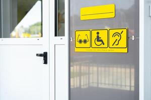 Accessibility signs displayed on an entrance door indicating facilities for the visually impaired, disabled, and hearing impaired photo