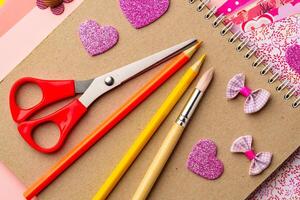 Craft supplies arranged on a tabletop featuring scissors, colored pencils, and decorative heart shapes created for a creative project photo