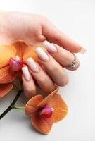 Woman hand with stylish trendy nude manicure holding orange orchid flowers photo