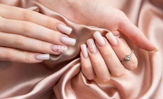 Woman showing stylish white nails with red glitter and diamond ring on silk fabric photo