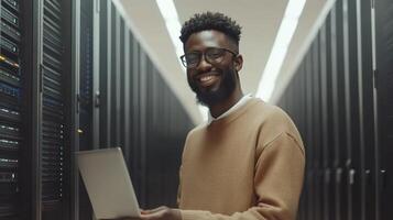 Man with beard and glasses operates laptop inside a data center filled with servers photo