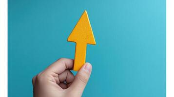 A hand is displaying a vibrant yellow arrow shape with a smooth finish against a blue backdrop photo