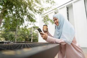Muslim woman enjoying coffee while using a smartphone in a business setting. photo