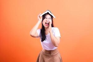 A woman with a book on her head with an orange background is yelling for help isolated on orange background photo