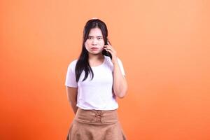 A woman with a phone is positioned against a solid orange background while making a call photo