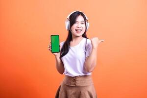 Young woman smiling, holding a phone with a green screen on an orange background photo