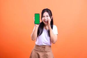Woman holding phone with green screen and shouting announcement on orange background photo