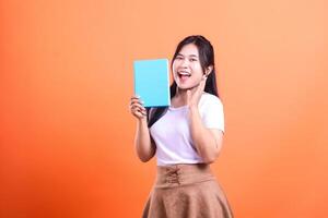 A woman is holding a book up with a surprised expression on an orange background while showing a book photo
