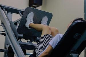 woman using leg press machine in gym. plant her feet on the machine platform, ready to push. The machine is made of metal and has a grey platform with diamond pattern photo