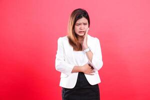 A woman with light brown hair wearing a white jacket and black skirt is touching her cheek, seemingly having a toothache, isolated on a red background photo