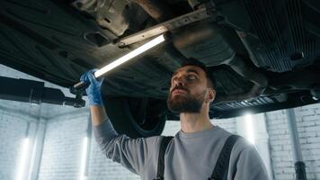Caucasian man professional mechanic in uniform repairman male engineer working underneath car check fix problem under automobile using flashlight light vehicle diagnostics garage service auto repair photo