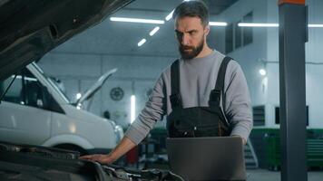 Caucasian man mechanic working in car service workshop fixing engine using laptop electronic diagnostics test repair vehicle automobile with computer technology buying online in auto shop warehouse photo