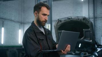 Professional mechanic Caucasian man in uniform male industrial worker technical mechanical engineer using laptop check automobile diagnostics auto system engineering work car maintenance in service photo