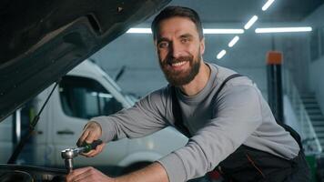 Car mechanic vehicle service worker working in workshop garage using wrench tool to repair engine open hood automobile adult Caucasian man auto engineer in technical uniform happy looking camera smile photo
