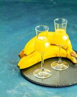Two glasses of banana liqueur resting on slate with fresh bananas photo