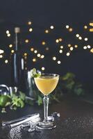 Yellow cocktail garnished with lime and mint on wet countertop with bokeh background photo