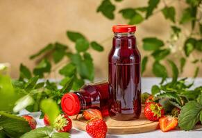 Two bottles of fresh strawberry juice resting on wooden board with ripe strawberries and mint leaves photo