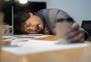 Asian tired staff officer man sleeping while using desktop computer having overwork project overnight in office. photo