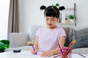 A sweet little girl is using colored pencils to draw and add color to her artwork on a paper. photo