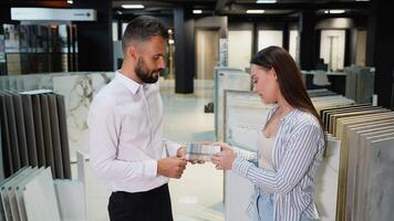 A friendly interaction between a sales consultant and a female customer in a tile showroom. The consultant explains tile options, helping her make an informed choice for her project video