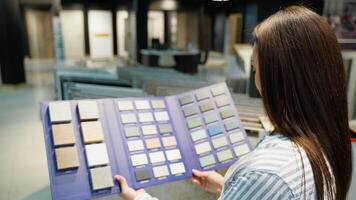 A woman browses through a palette of tile color samples in a showroom, carefully considering options to find the perfect match for her home decor and design needs video